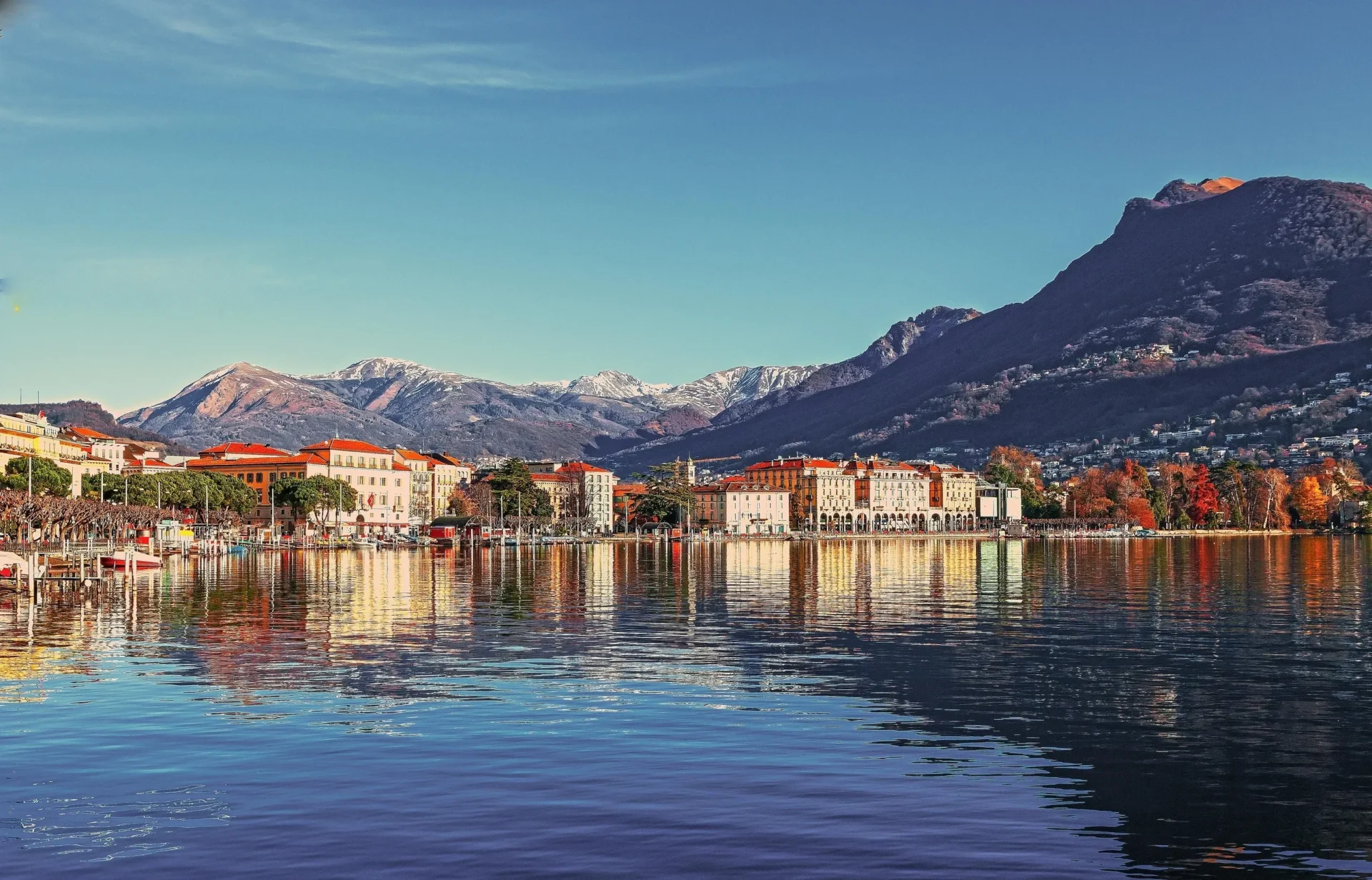 A painting of the mountains and water in front of some buildings