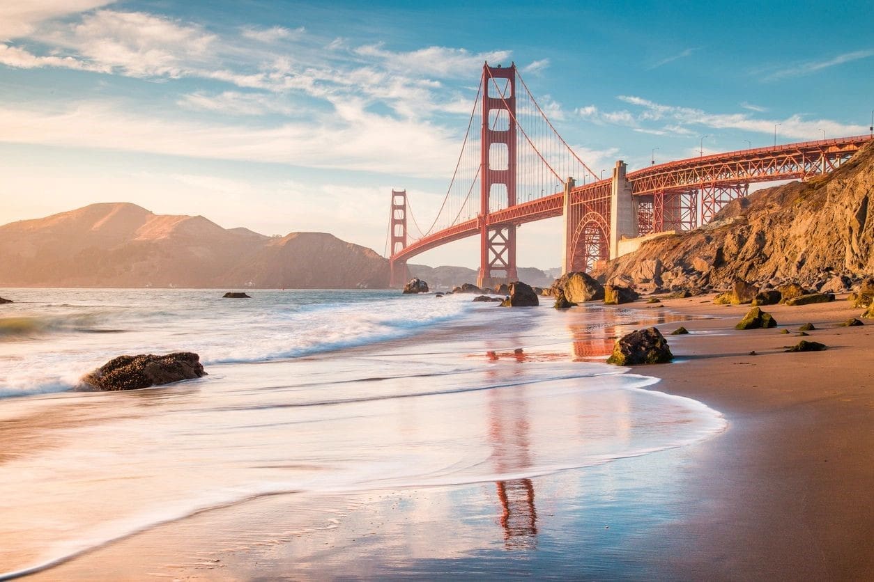 A beach with people swimming in the water and a bridge