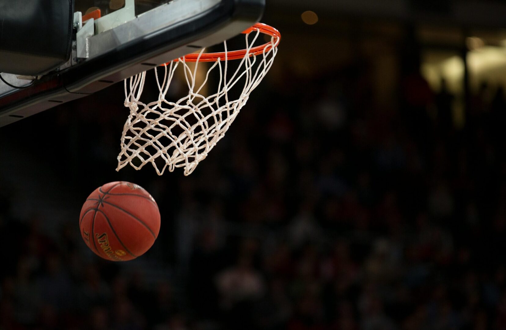 A basketball is going through the net and into the hoop.